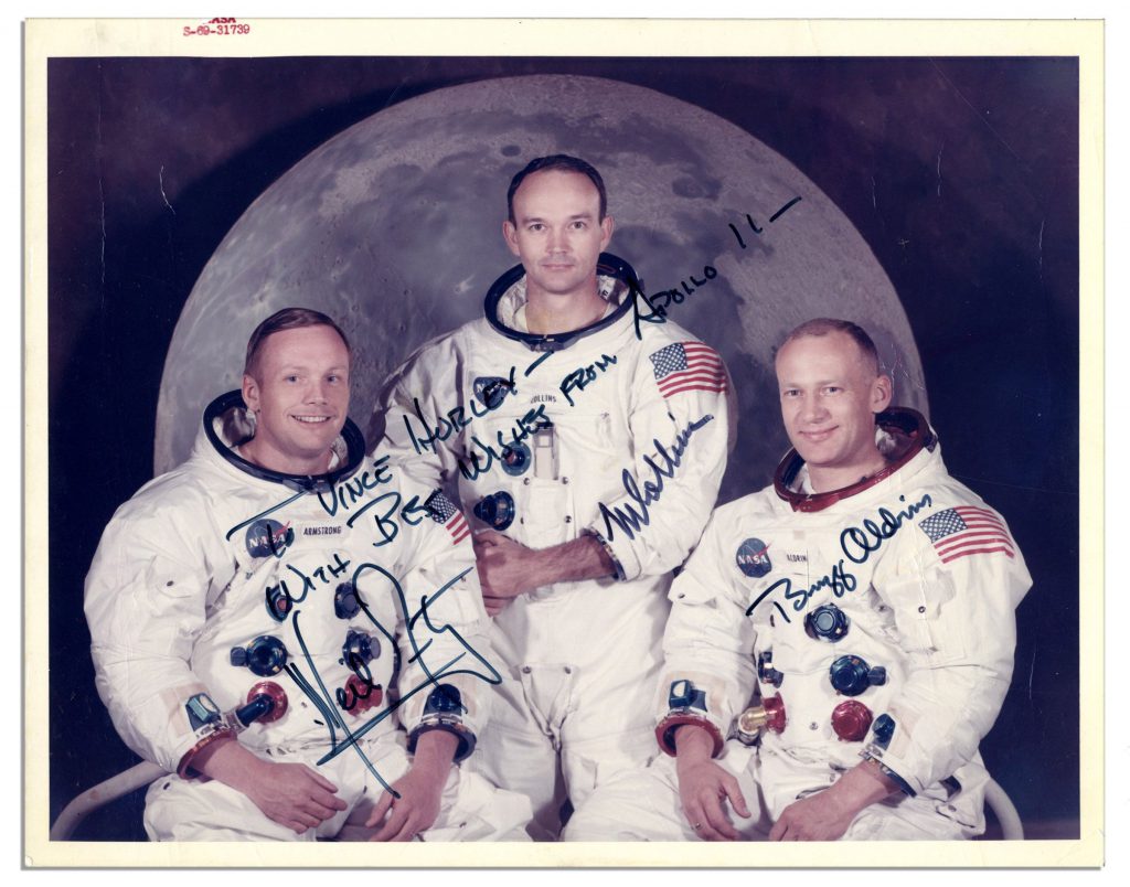Apollo 11 crew in posed in spacesuits. All sign their name near images.
