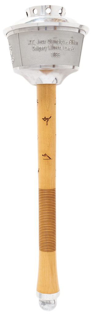 1988 Calgary Winter Olympics torch. A nearly two foot long torch consisting of a maple wood handle with small engraved images of winter sports. An aluminum bowl sits at the top and is engraved with the text "XV Olympic Winter Games / Calgary Alberta Canada / 1988'' in both English and French.