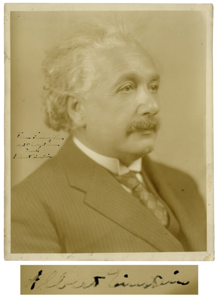 3/4 portrait of Albert Einstein dressed in a suit jacket and tie. Einstein signs along left center.