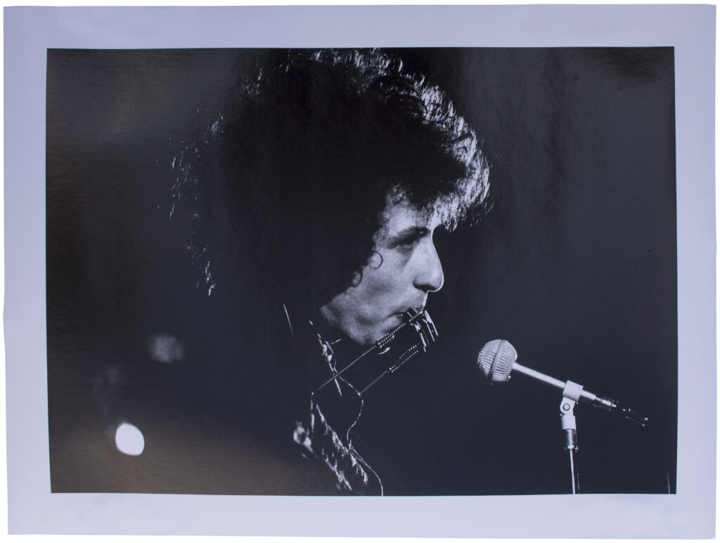 Bob Dylan performing with a harmonica in front of a mic.