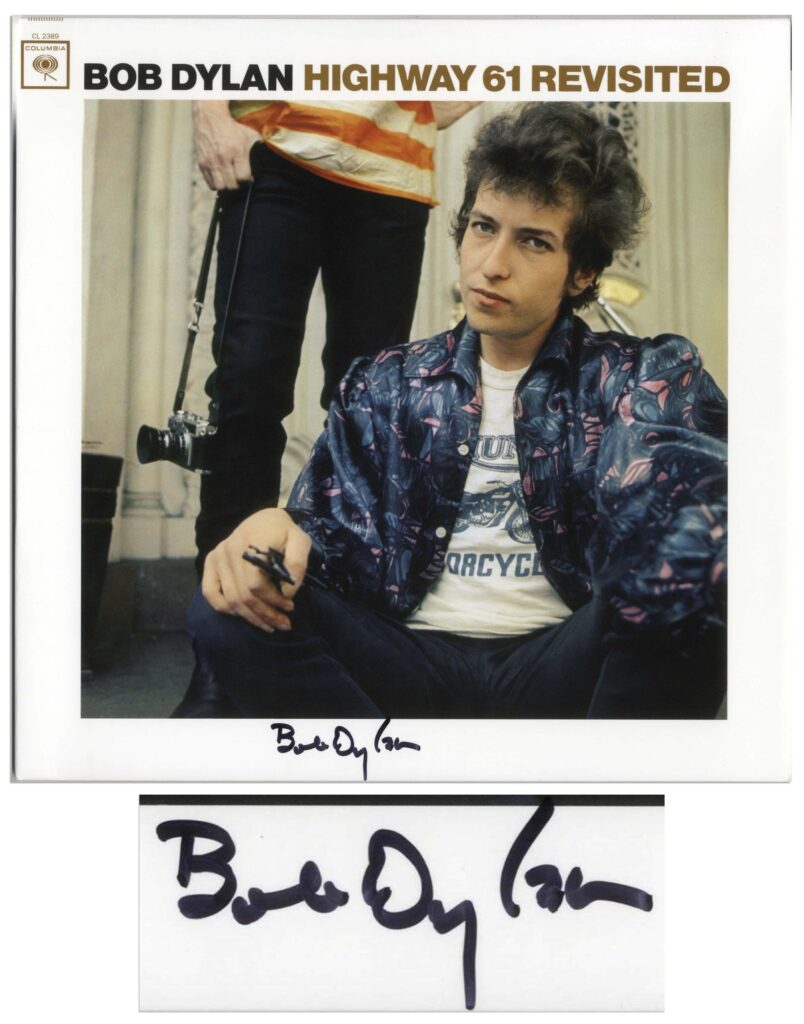 Color image of Bob Dylan sitting on a stoop looking straight ahead. Another male figure is visible behind him. Dylan signs along bottom margin.