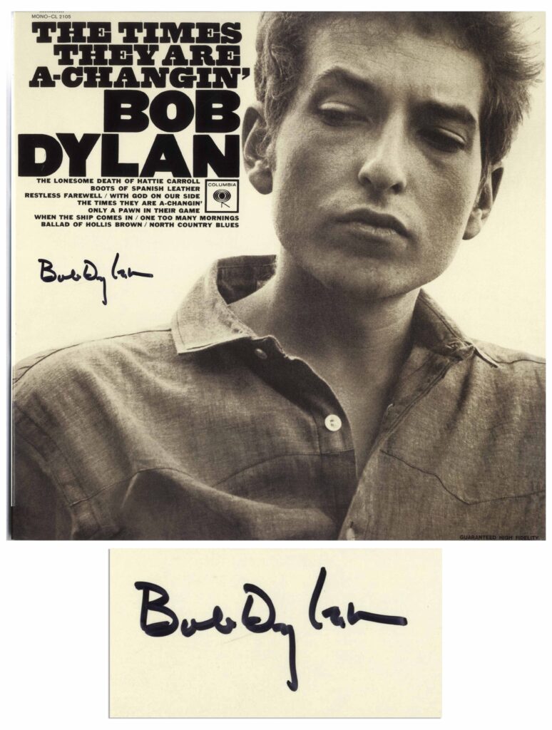 Black and white headshot of Bob Dylan wearing a button up and glancing down to the side. Dylan signs on left.
